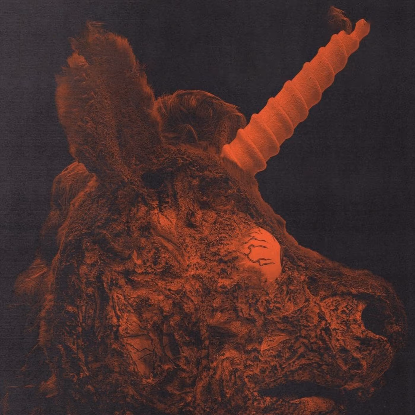 Close-up of a decayed unicorn mascot head with matted fur, a cracked glowing eye, and a long spiral horn under ominous red lighting.