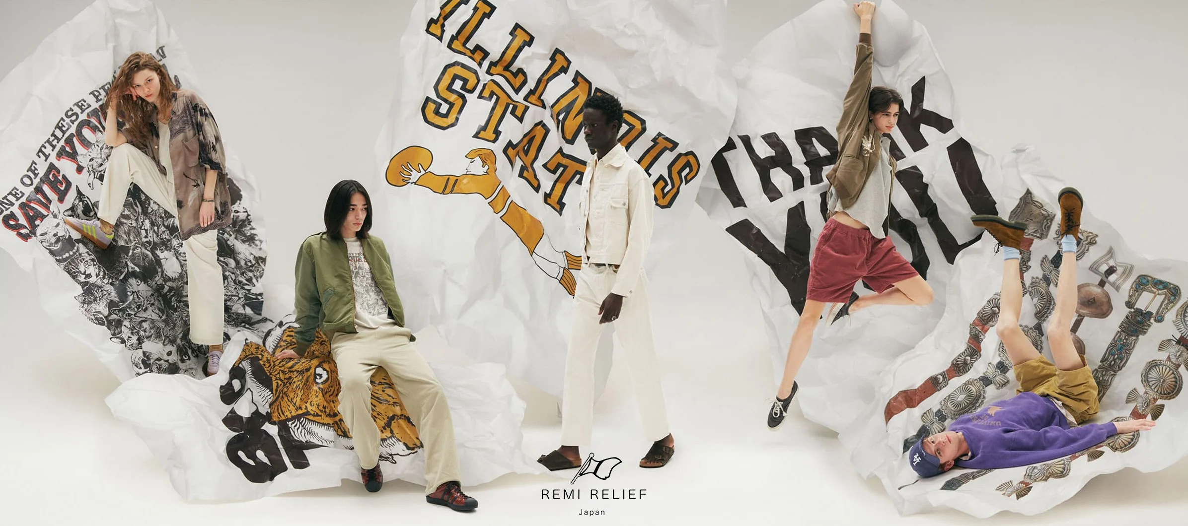 REMI RELIEF Japan campaign image showing five models styled in oversized workwear-inspired pieces including a green bomber jacket, cream denim jacket, tan trousers, and a purple hoodie, posed against an oversized crumpled paper backdrop printed with collegiate-style lettering, vintage cat and tiger graphics, and western-style silver concho belt artwork, with the REMI RELIEF Japan logo centered at the bottom.