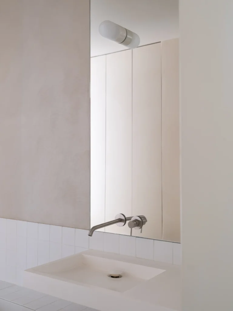 Minimal bathroom vanity with integrated white sink, wall-mounted stainless steel faucet, mirrored cabinet, and soft neutral finishes accented by white tile