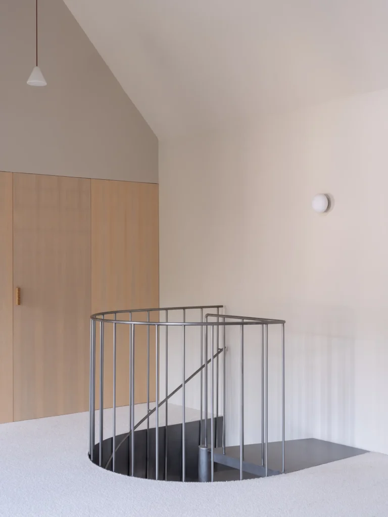 Upper landing with a circular stair opening enclosed by a black metal railing, light oak cabinetry, vaulted ceiling, and understated modern lighting