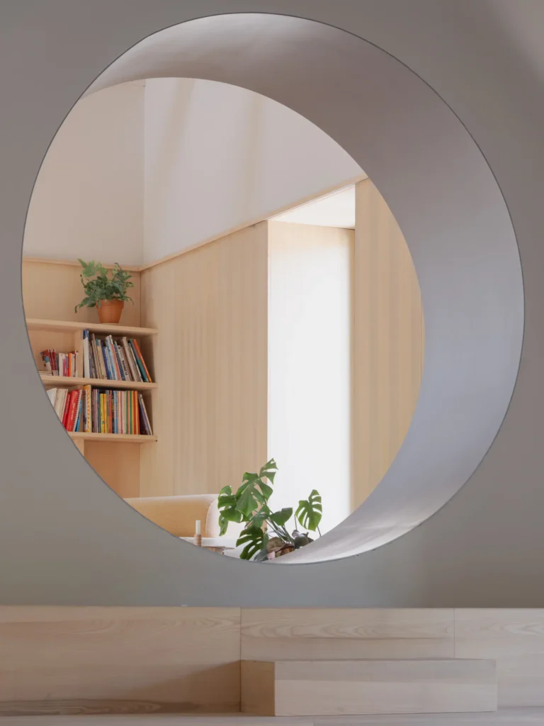 Circular interior opening frames a cozy reading nook with built-in oak bookshelves, potted plants, and warm natural wood finishes in a contemporary home