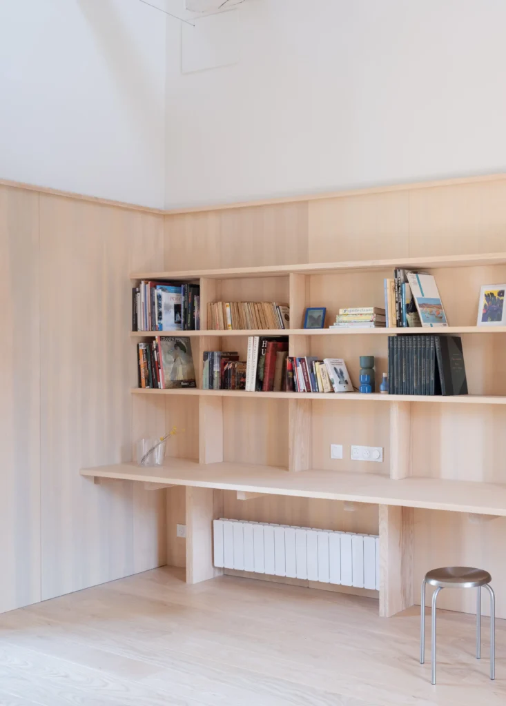 Built-in oak shelving and desk lined with books and decorative objects create a minimalist home library and workspace with clean architectural detail