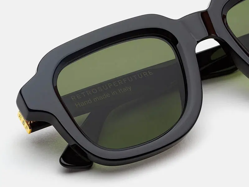Close-up of RSF Blades Series 2026 sunglasses featuring a glossy black acetate frame, olive green lenses, gold-tone temple hardware, and handcrafted branding visible through the lens.
