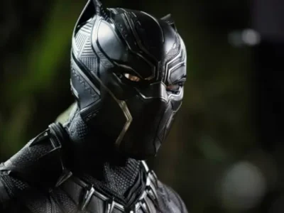 Black Panther in a close-up promotional image wearing the iconic black vibranium suit and panther mask with silver accents. The cinematic portrait highlights the textured armor, angular facial detailing, and vigilant gaze against a softly blurred dark green background, emphasizing the character's technologically advanced Wakandan design