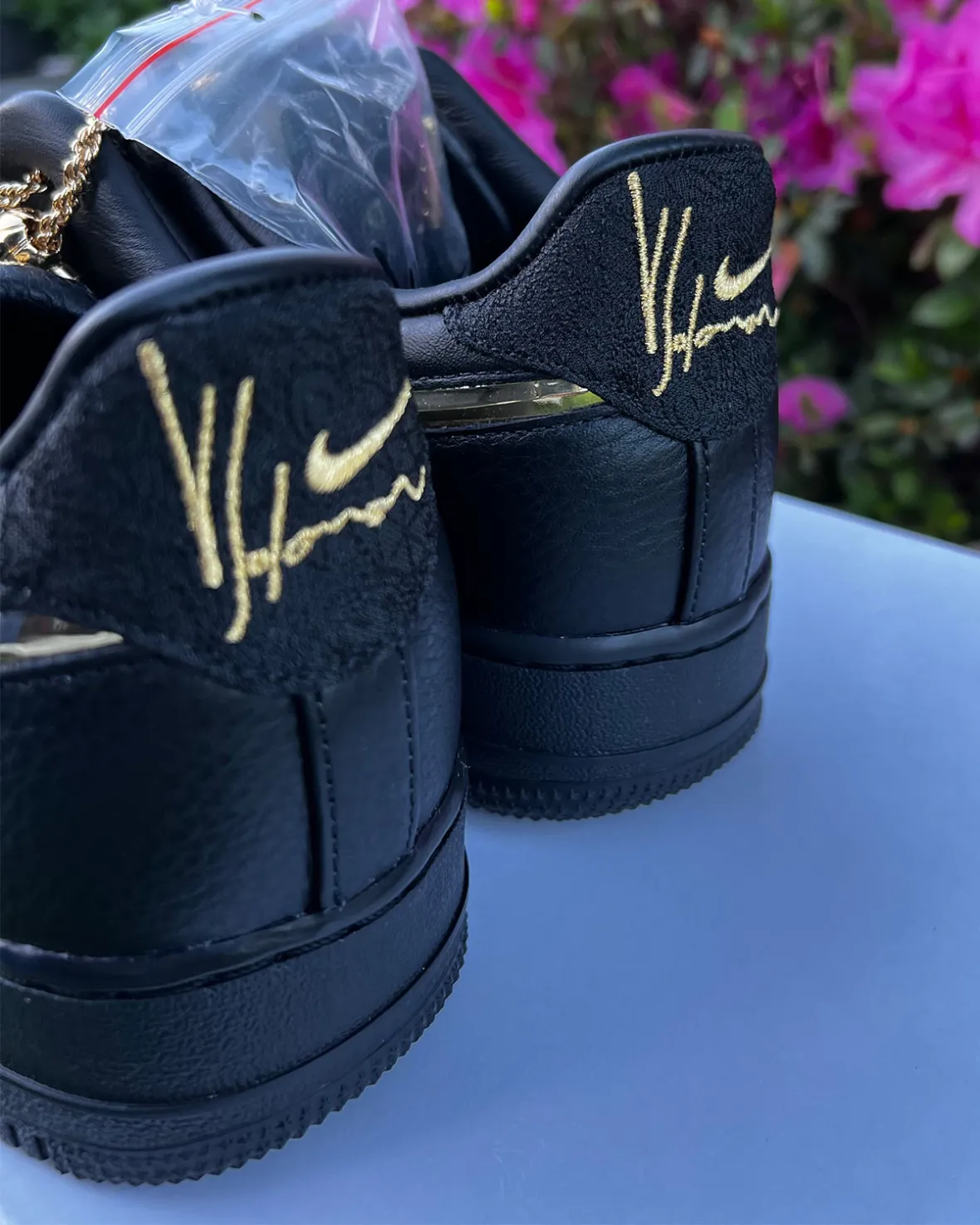 Rear view of the Victor Solomon x Nike Air Force 1 highlighting embroidered gold Yoon signature branding across the black suede heel tabs, premium black leather construction, and luxury-inspired detailing against a floral backdrop.