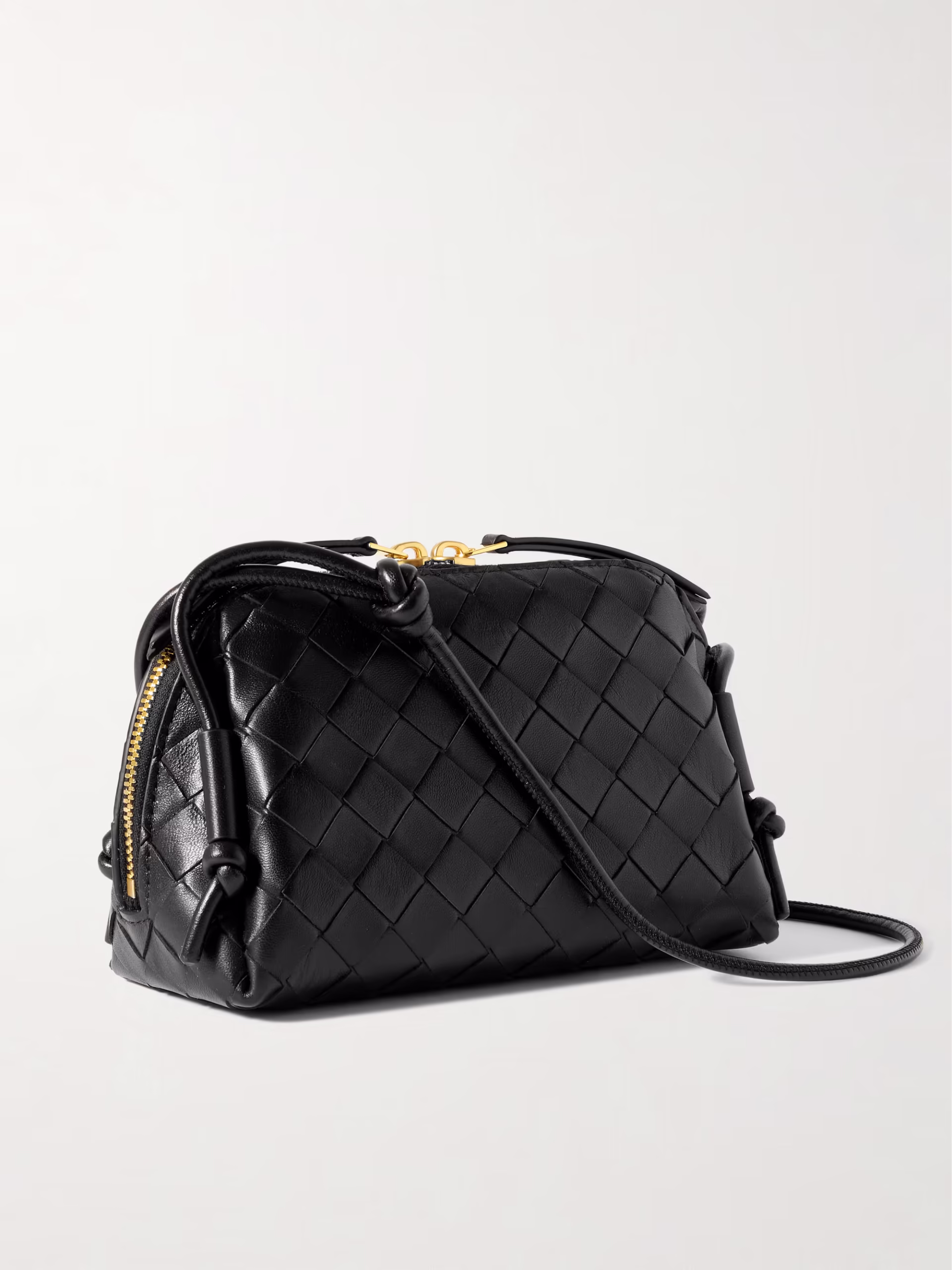 Black intrecciato woven leather crossbody bag with a softly structured silhouette, slim adjustable shoulder strap, gold-tone zipper hardware, and knotted strap details, photographed against a clean light background.