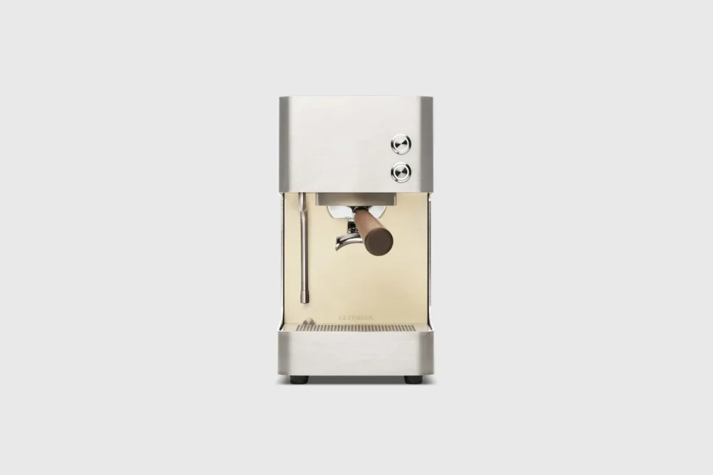 Front view of the compact stainless steel espresso machine showing dual control buttons, steam wand, wooden portafilter handle, and illuminated brewing area against a neutral background