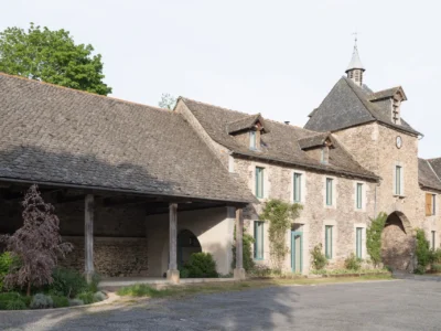 Historic stone residence with slate roofs, arched entrance tower, teal-framed windows, and landscaped courtyard blending traditional rural architecture with modern renovation