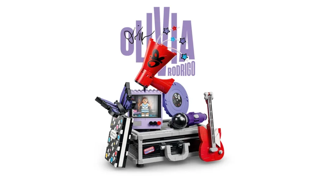 LEGO Olivia Rodrigo playset displayed on a silver briefcase. Features a purple TV monitor with minifigure, red megaphone, purple microphone, red electric guitar, purple vinyl record, and various music-themed accessories. Large "OLIVIA RODRIGO" logo with signature in the background