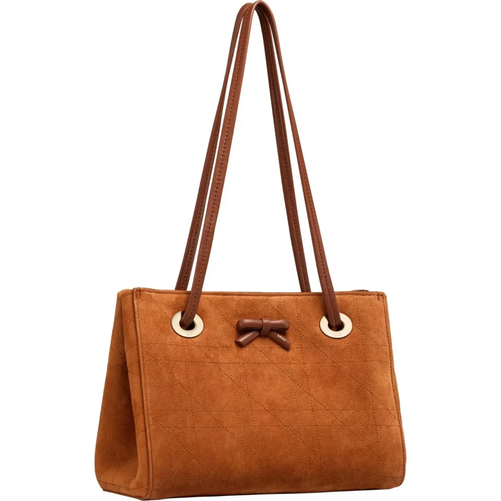 Tan suede quilted tote bag with long leather shoulder straps, gold grommet details, and a small leather bow accent on the front