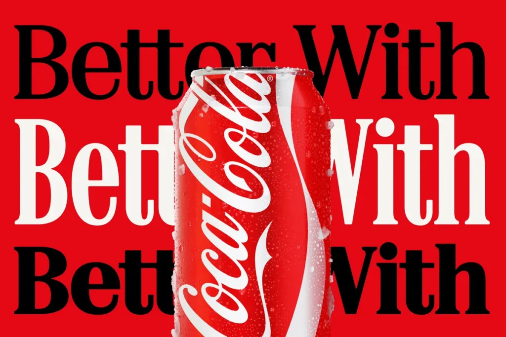 Chilled Coca-Cola can covered in condensation and ice crystals placed in front of a bold red background with the phrase "Better With" repeated in large black and white serif lettering, emphasizing Coca-Cola's iconic branding and campaign aesthetic
