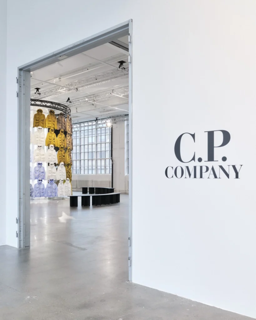 Entrance to the C.P. Company exhibition, with the black C.P. Company logo beside a wide doorway revealing colorful archival jackets inside
