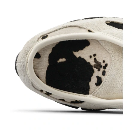 Close-up top view of a cream suede shoe with a black and cream cow-print footbed.