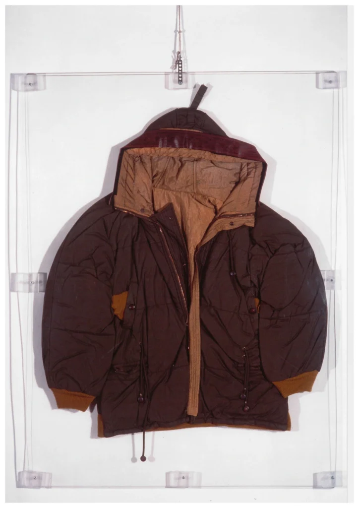 Vintage C.P. Company hooded brown jacket displayed flat against a transparent acrylic panel