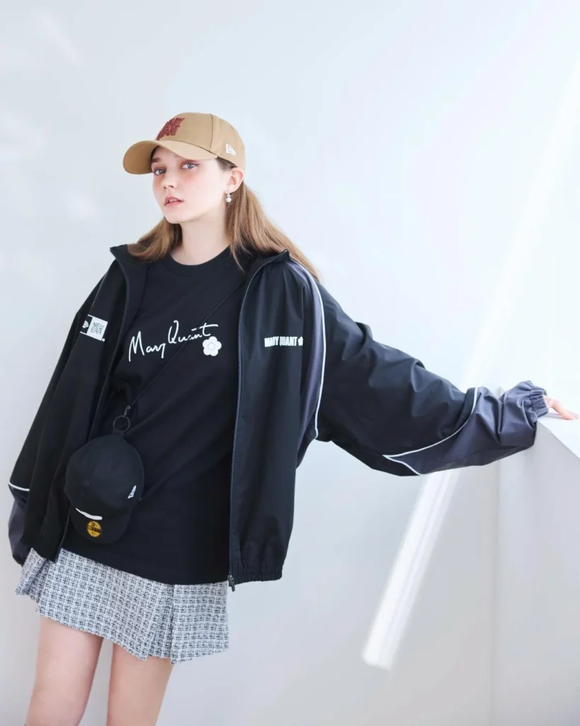 Model Wearing Mary Quant X New Era Cap, Black Shirt And Track Jacket In Studio