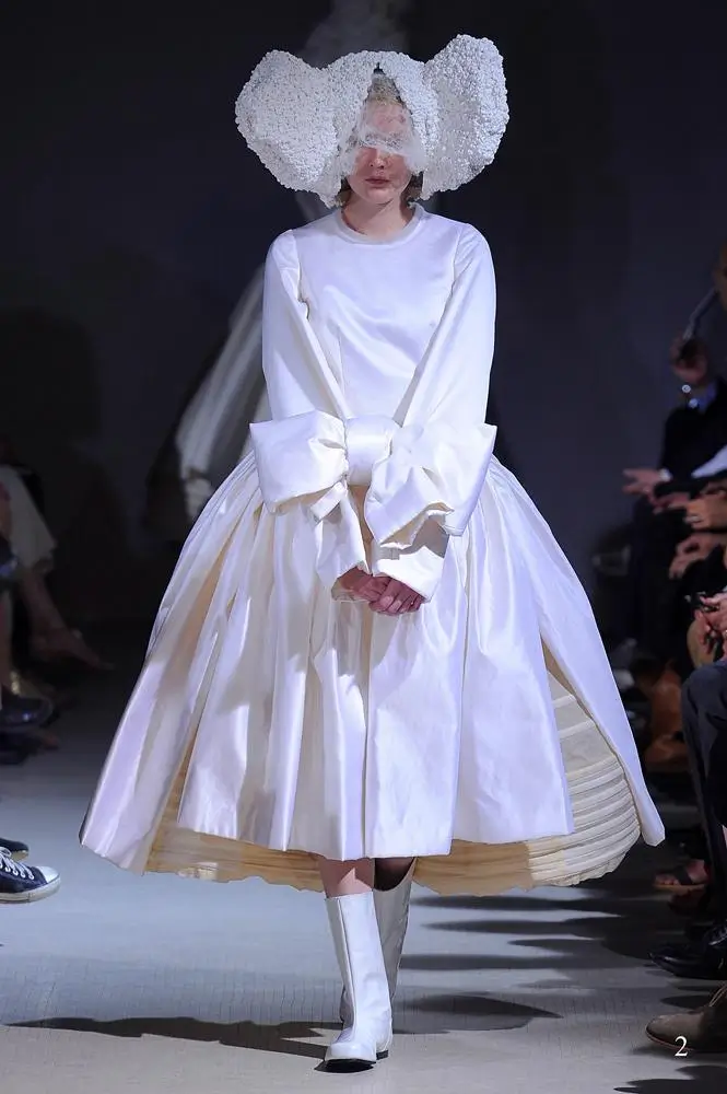 Model wearing a voluminous white Comme des Garçons dress with oversized cuffs and a sculptural cloud-like headpiece.