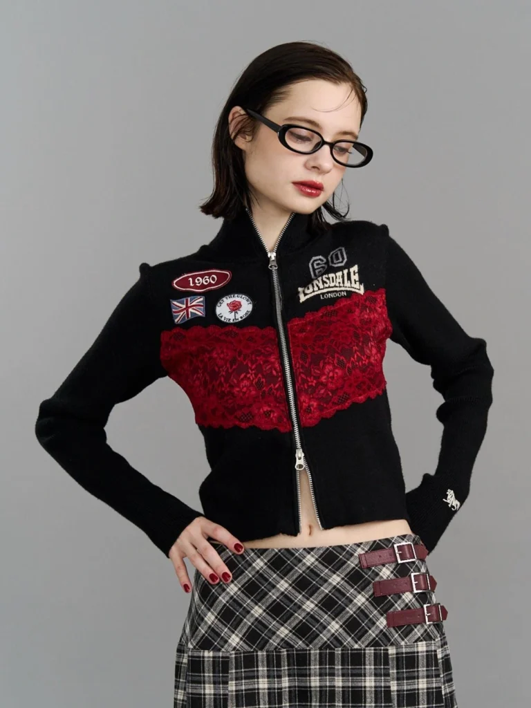Close-up of the checkerboard fringed scarf with red "1960" patch, worn over a black top with a plaid skirt