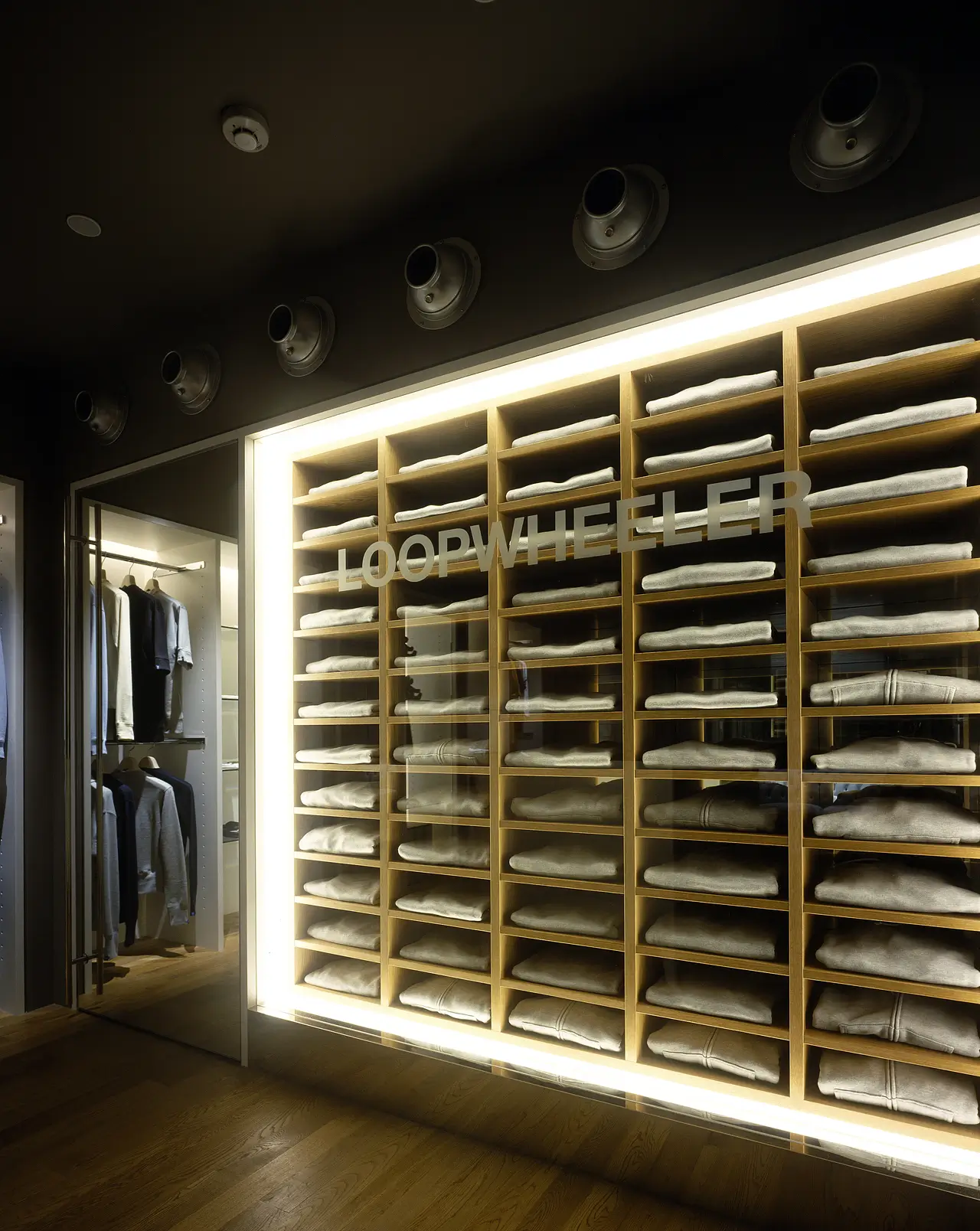 LOOPWHEELER store interior with illuminated wooden shelving filled with neatly folded gray garments.