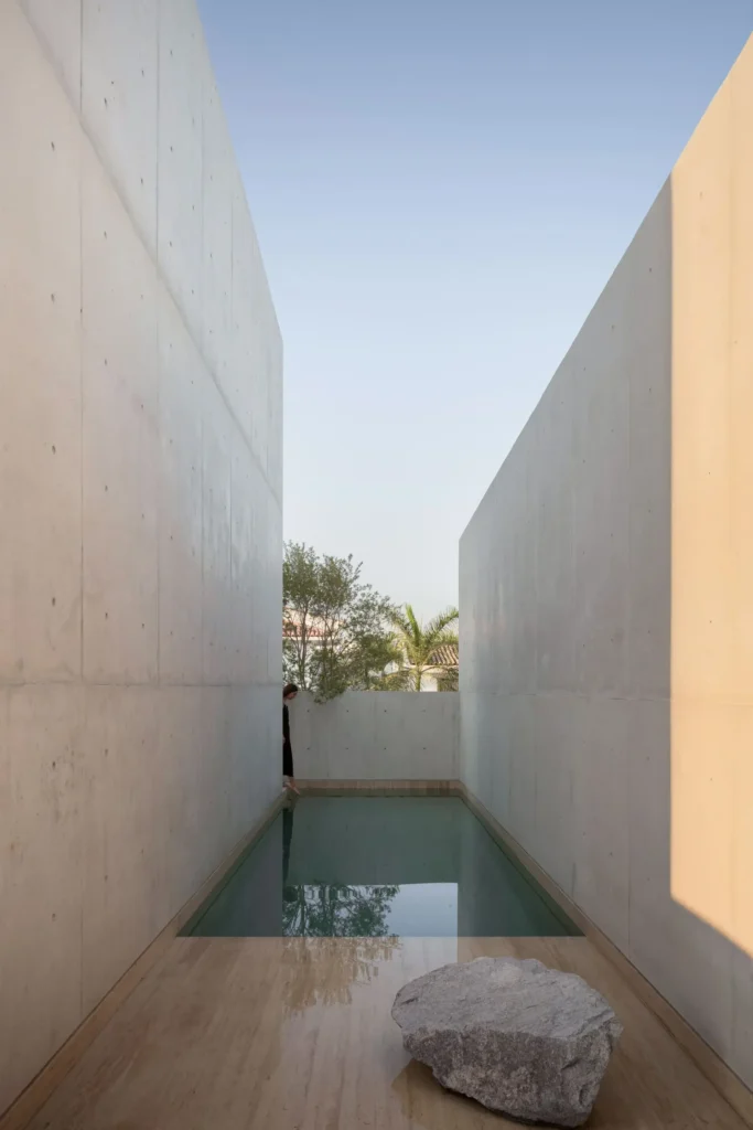 Min reflect pool bordered by tall concrete walls, calm water, and a sculpture stone emphasize symmetry and reflection