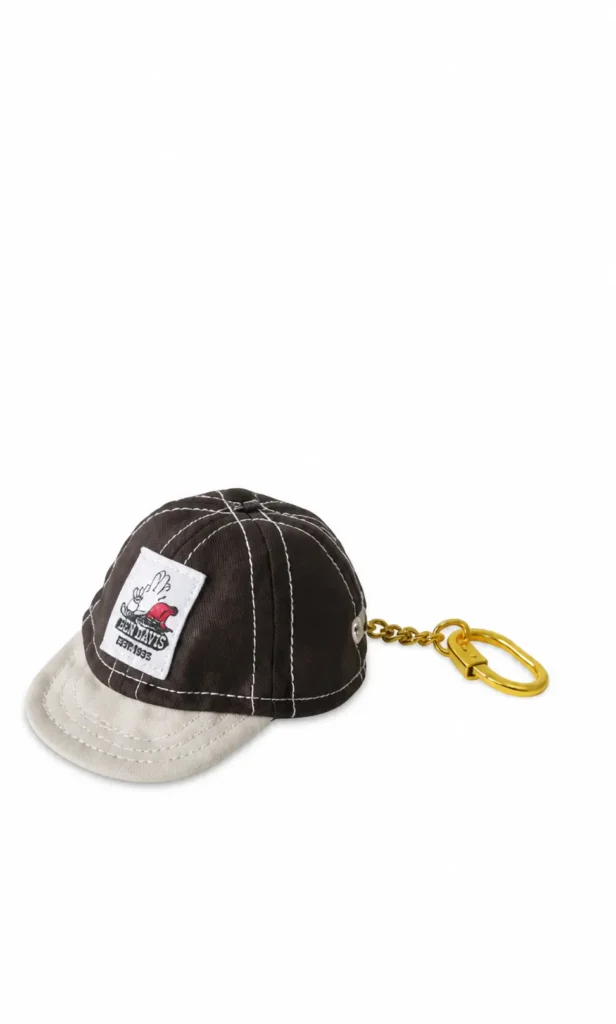 Mini black and cream cap keychain with contrast stitch, graphic patch, and gold-tone clasp
