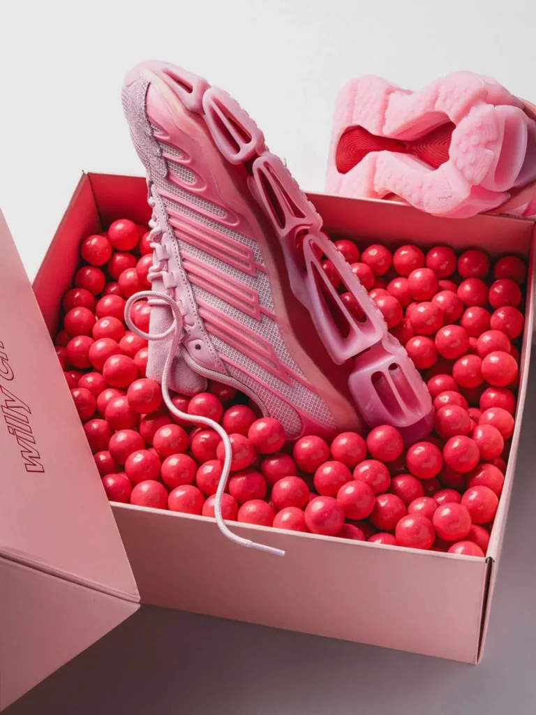 Pink adidas x Willy Chavarria shoe displayed inside an open presentation box filled with glossy red gumballs, highlighting the sculpture sole profile