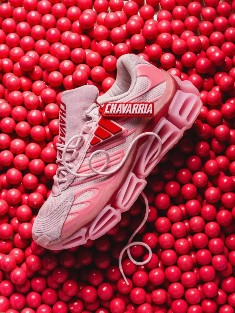adidas x Willy Chavarria pink shoe resting on glossy red gumballs, highlighting the removable co-branded hangtag and oversized hollow sole