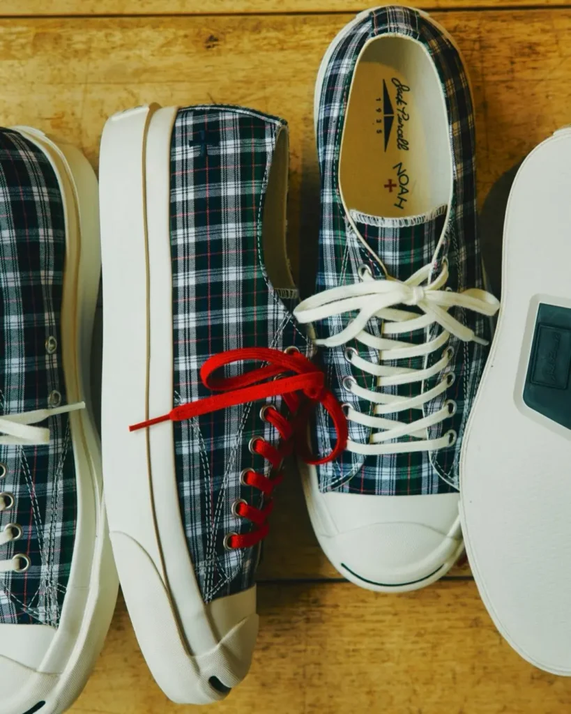Assort of Noah x Jack Purcell plaid low-top shoes arrange on a wooden floor, feature off-white rubber sole with contrast red and white lace
