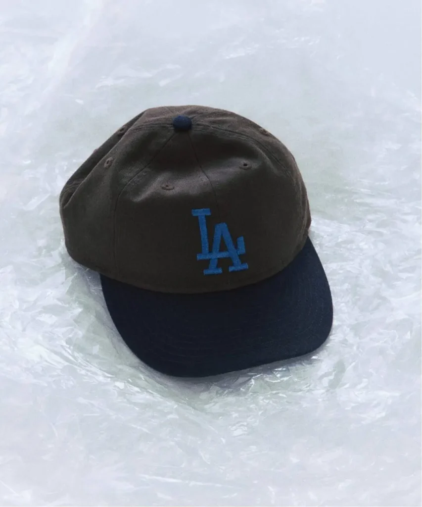 Dark baseball cap with blue LA logo and brim, resting on crinkled translucent plastic surface