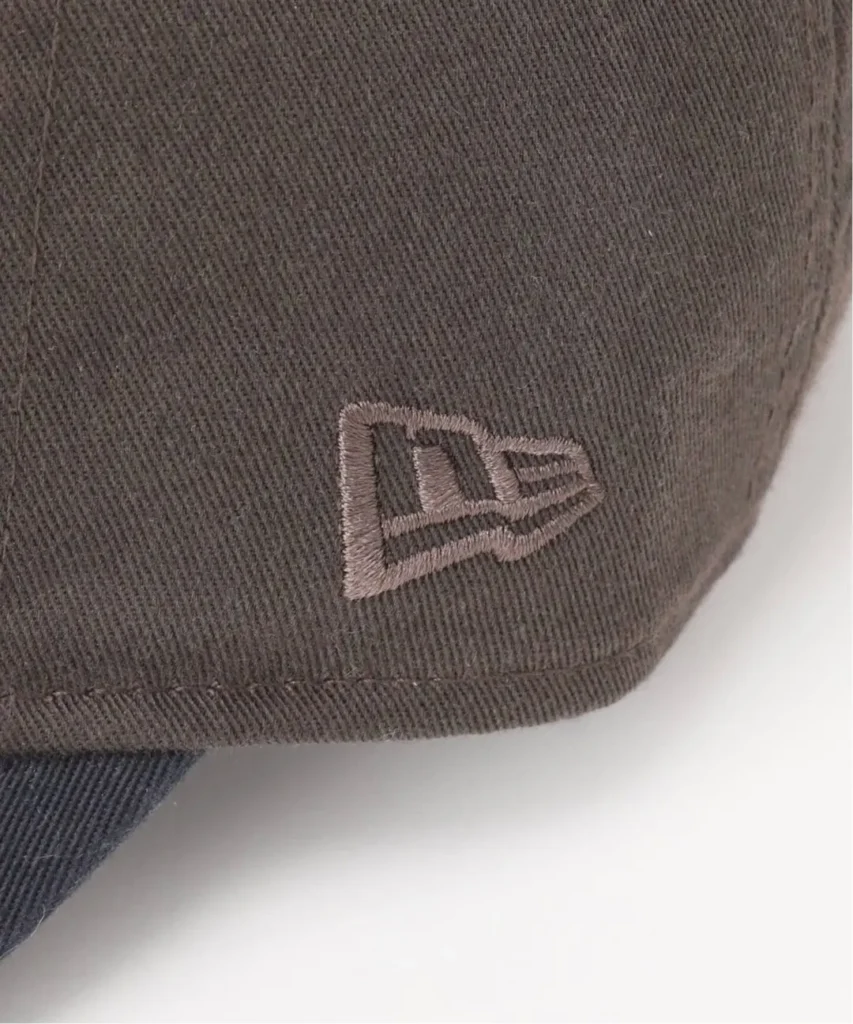 Close-up of a dark gray New Era cap with an embroidered logo and curved brim on a white background