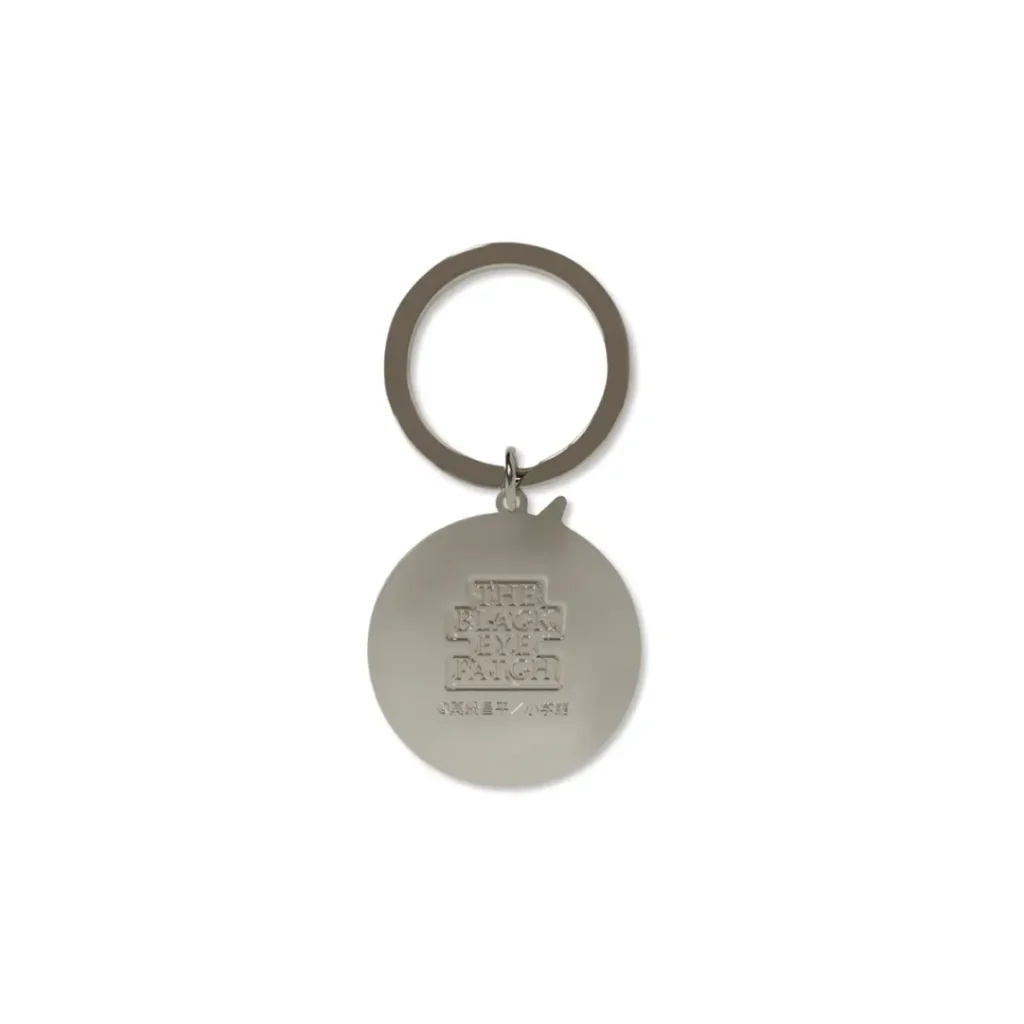 Back of the keychain, engraved with the stacked "THE BLACK EYE PATCH" logo and a small manga credit line