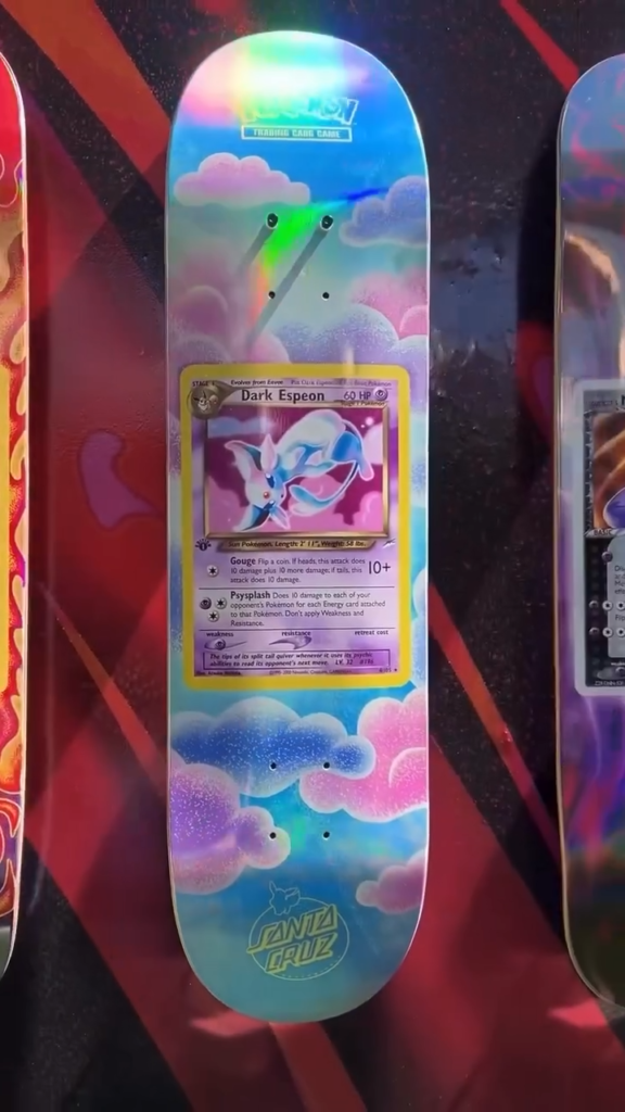 Santa Cruz skateboard deck featuring a Dark Espeon Pokémon card on a colorful cloud design