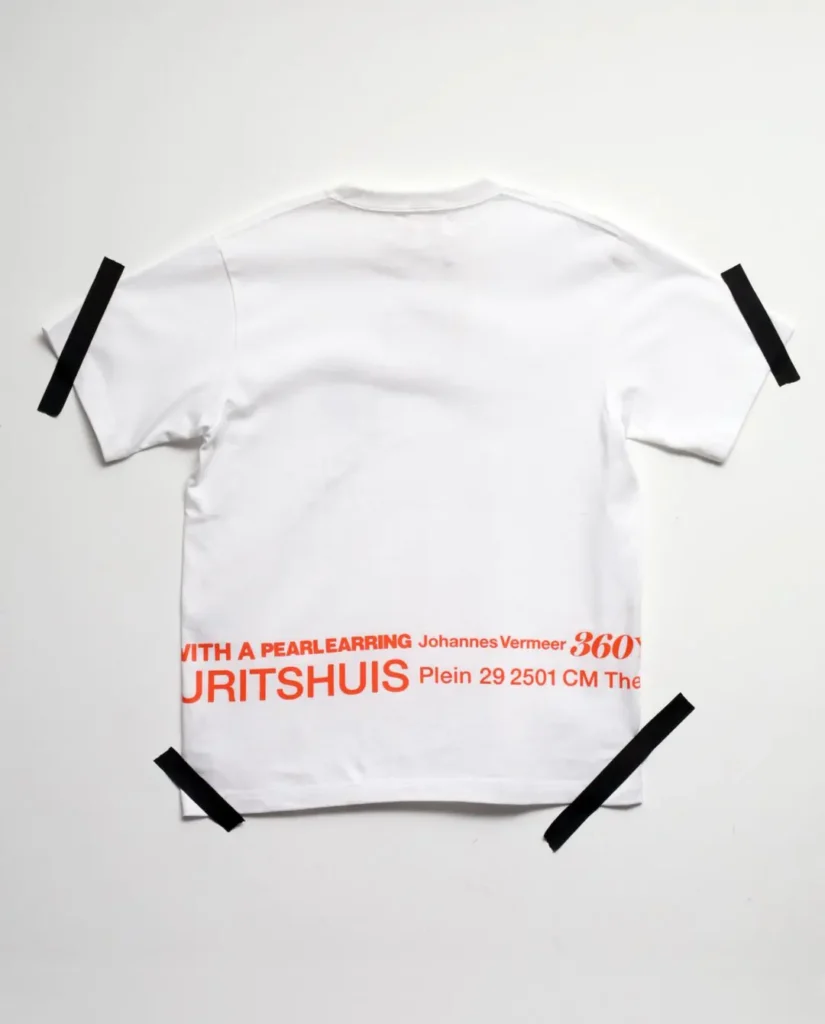 Back of a white Tee feature oversized orange typography referencing Johannes Vermeer, the Mauritshuis museum, and Girl with a Pearl Earring