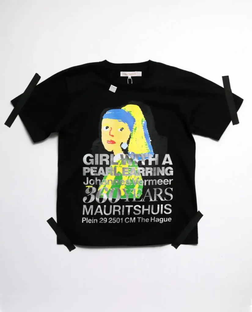 Black T-shirt with a colorful abstract reinterpretation of Girl with a Pearl Earring overlaid with bold silver commemorative typography
