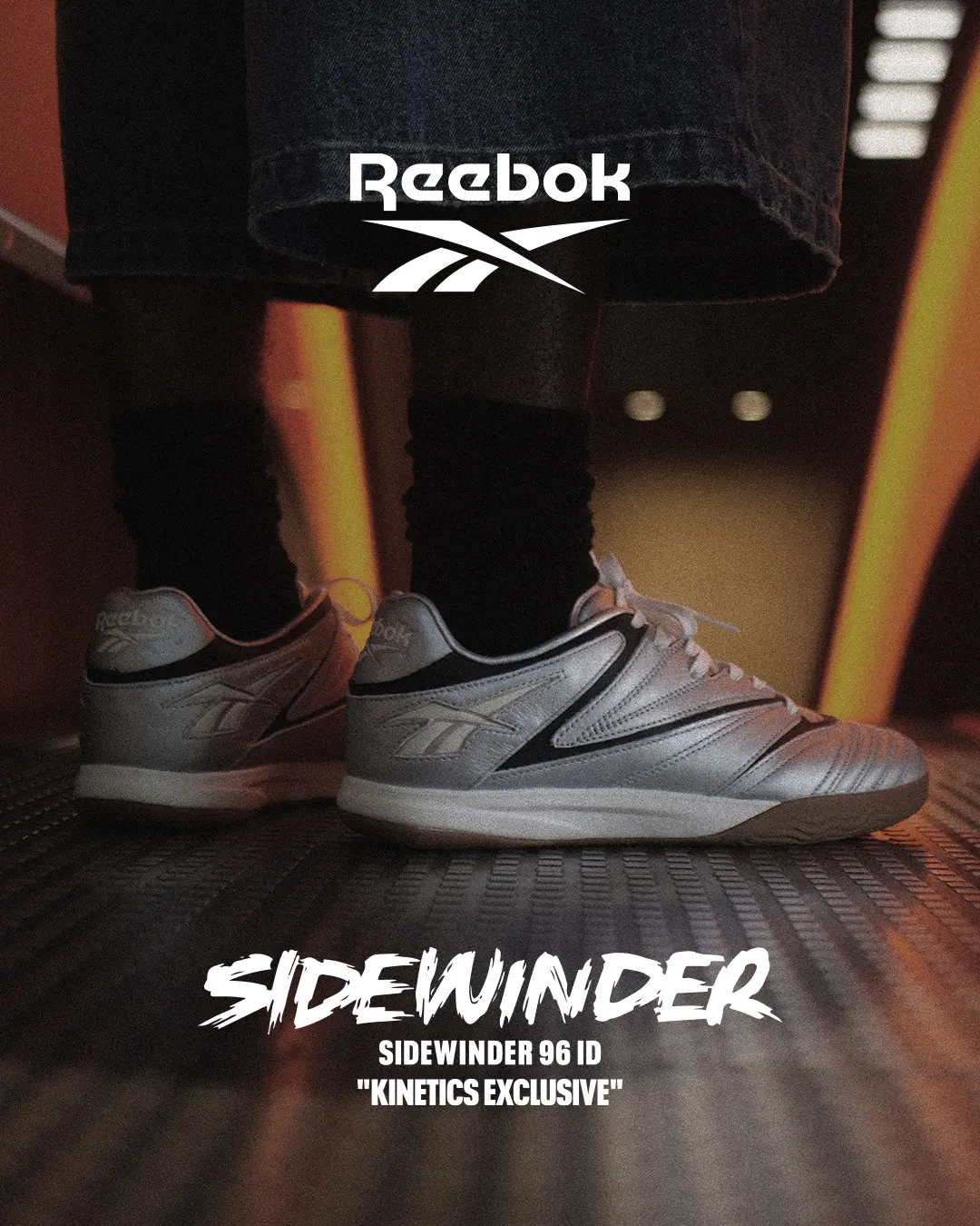 Reebok Sidewinder 96 ID campaign image showing metallic silver shoes worn with black socks and dark shorts in a dimly lit urban setting.