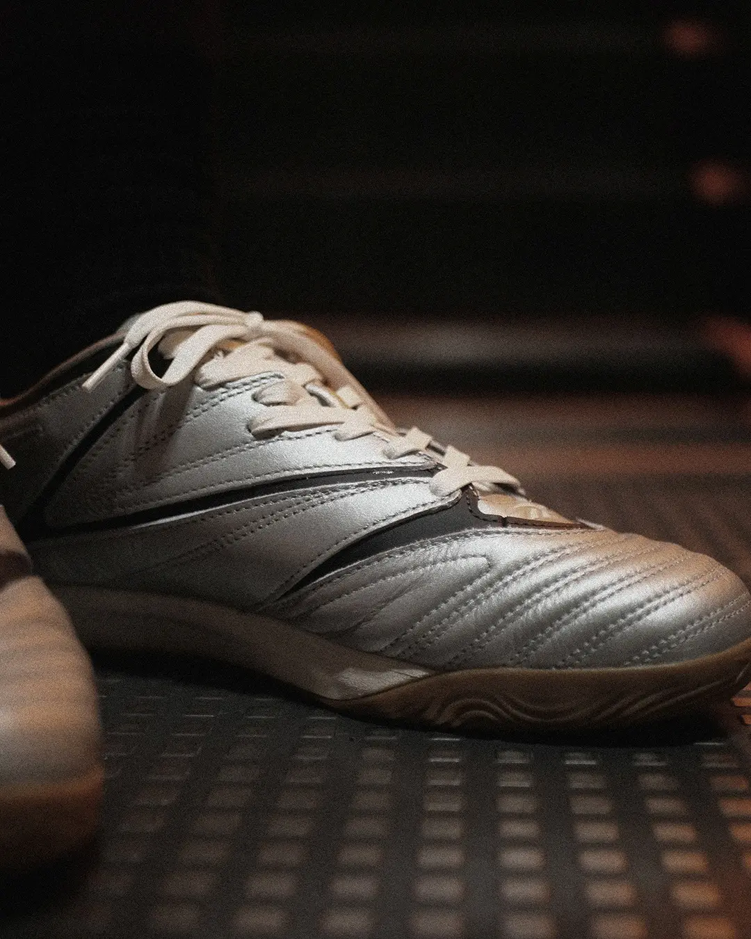 Close-up of a metallic silver Reebok Sidewinder 96 ID shoe with black detailing, white laces and a gum outsole.