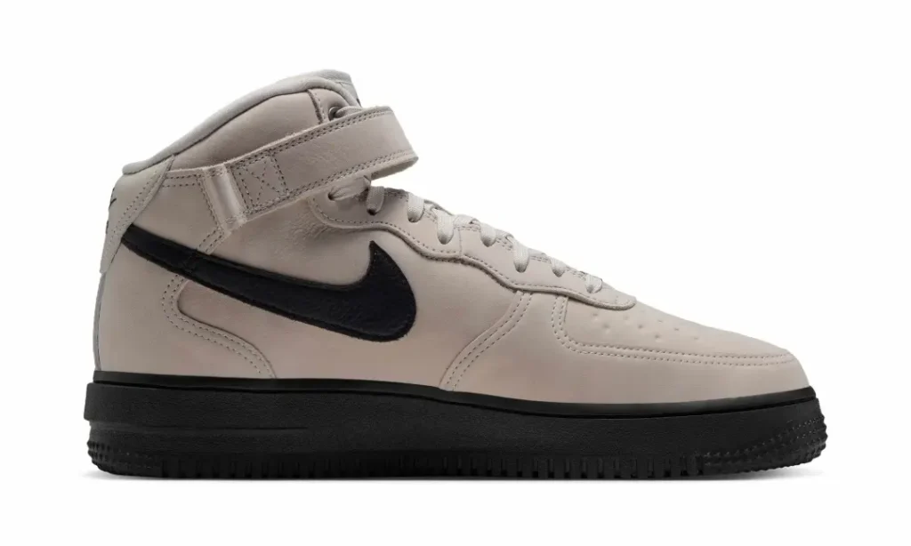 Medial side profile of the beige Nike Air Force 1 Mid feature a black Swoosh, ankle strap and black sole