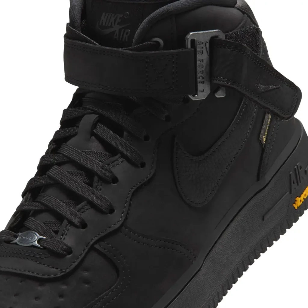 Close-up of the black Nike Air Force 1 Mid show the ankle strap buckle, texture Swoosh, lace and Vibram brand