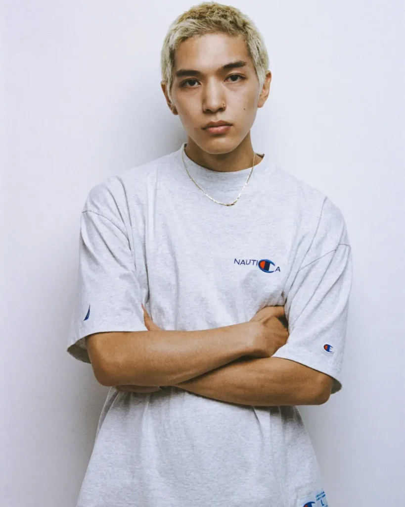 Model with short bleach hair wear an oversized light gray Champion x Nautica Tee with embroider chest brand and sleeve detail
