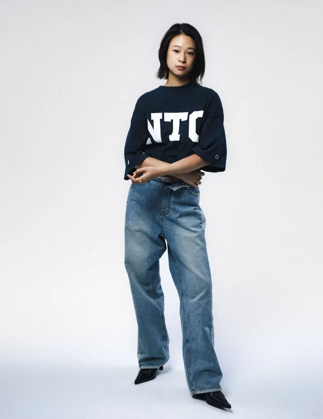 Model Wearing An Oversized Navy Champion X Nautica NTC Graphic T-Shirt With Relaxed Blue Jeans And Pointed Black Shoes.