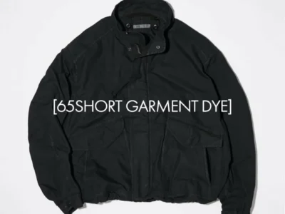 Black garment-dyed short jacket with stand collar, concealed zip front, and oversized flap utility pocket