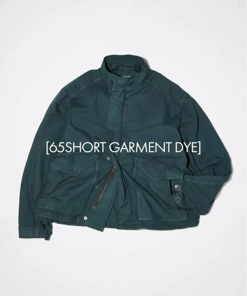 Deep teal garment-dyed utility jacket with a cropped silhouette, snap-and-zip front, flap cargo pockets, and adjustable cuff