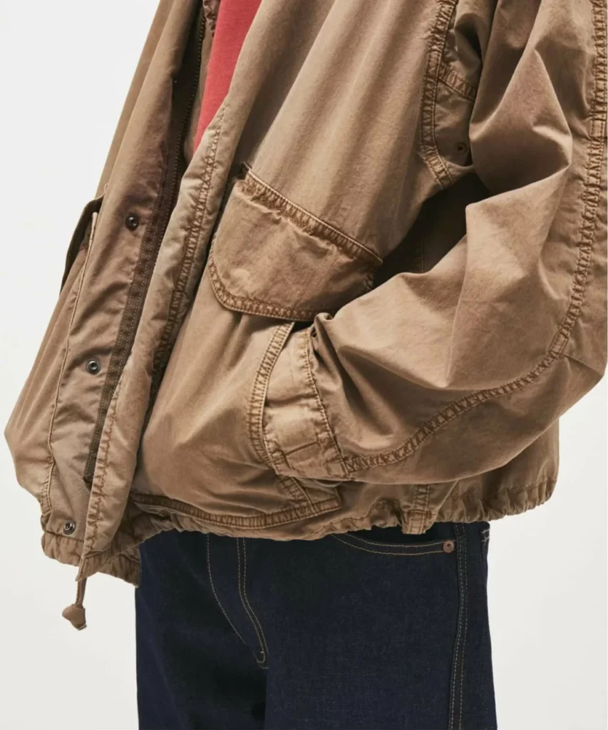 Close-up of the khaki jacket highlighting the garment-dyed fabric, oversized flap pocket, elastic hem, and rugged stitching detail