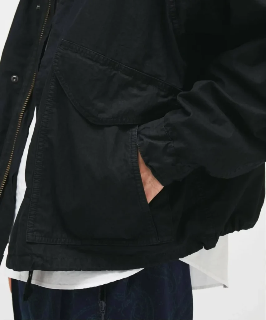 Close-up of the black jacket show the oversized flap pocket, concealed hand pocket, zip closure, and garment-dyed cotton texture