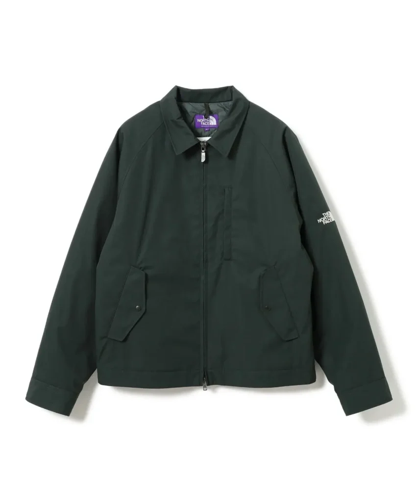 Front view of a dark forest green The North Face Purple Label jacket with a pointed collar, zip closure, flap pockets, and embroidered sleeve brand