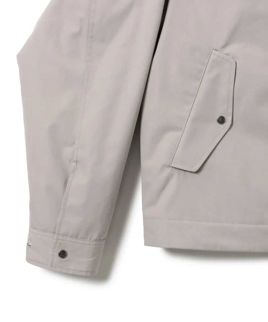 Detail of the light beige jacket highlighting the adjustable snap-button cuff and angular flap hand pocket