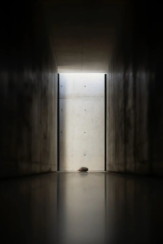 Min bedroom with expose concrete walls, low platform bed, floor-to-ceiling glass, and a peaceful courtyard framed by a curve architecture open