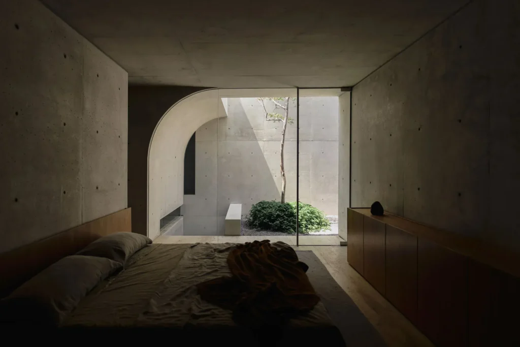 Quiet courtyard enclosed by tall concrete walls with a slender tree, gravel landscape, and sculpture boulder create a serene outdoor retreat