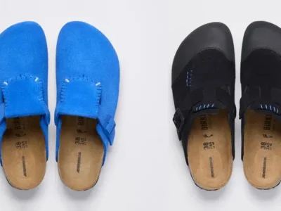 Blue and black Birkenstock clogs displayed side by side on a white background, featuring suede uppers, buckled straps, visible stitch, and cork footbed