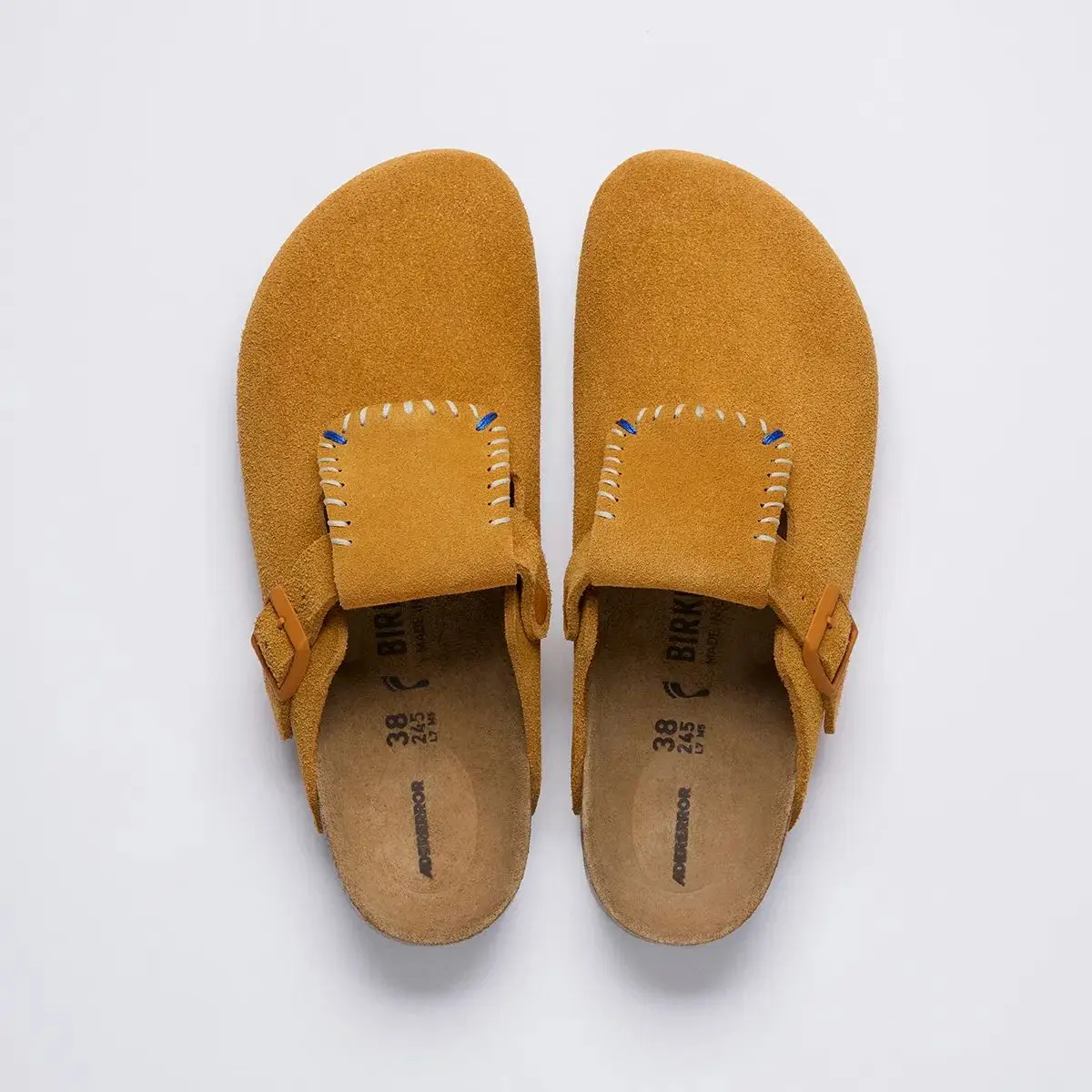 Brown suede Birkenstock clogs viewed from above, featuring stitched tongue panels, matching side buckles, and contoured cork footbeds.