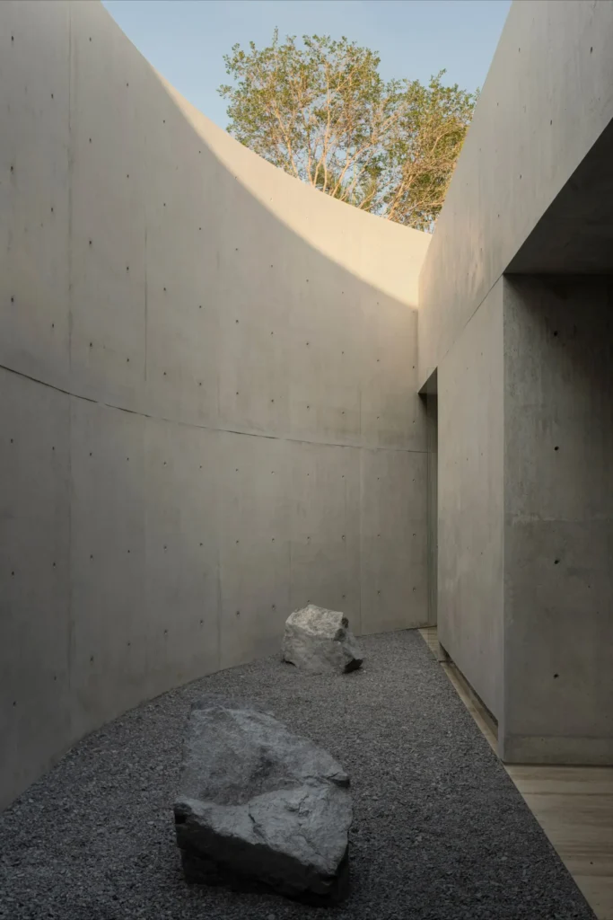 Min bedroom overlookia curve enclosed courtyard through full-height glass, featuring concrete walls, warm wood accents, and soft natural light